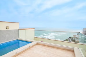 Ein Pool auf dem Dach mit Glasgeländer, freier Blick auf den Ozean und eine Stadtlandschaft im Hintergrund.