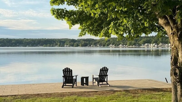 Vista al lago con dos sillas Adirondack y una pequeña mesa en un área pavimentada.