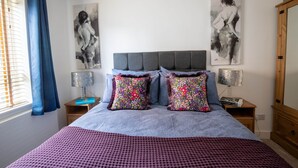 Ein Schlafzimmer mit einem Bett, zwei Nachttischen, einem Spiegel und Kunstwerken an der Wand.