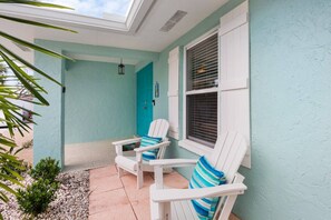 A covered outdoor seating area with two white Adirondack chairs, one with a striped cushion. - Mermaid Cove | Backyard Dream: Putting Green, Pool (Siesta Key)