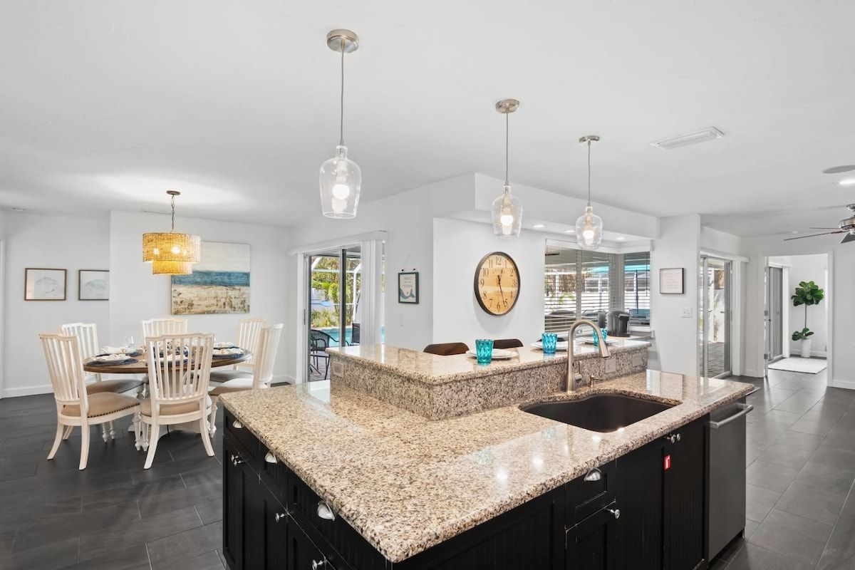 A modern kitchen with a granite island, black cabinetry, and pendant lighting.