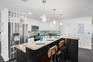 A modern kitchen with a stainless steel refrigerator, a microwave, and a bar area. - Mermaid Cove | Backyard Dream: Putting Green, Pool (Siesta Key)