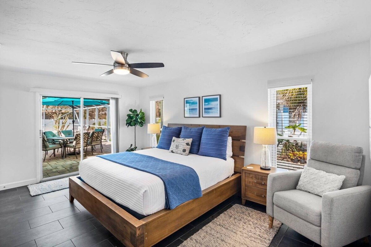 A bedroom with a bed, a ceiling fan, a nightstand, a chair, and a view through a window.