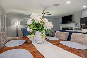 Una mesa de comedor con un jarrón de flores, una camino de mesa blanco y un ventilador de techo en una cocina y comedor modernos.