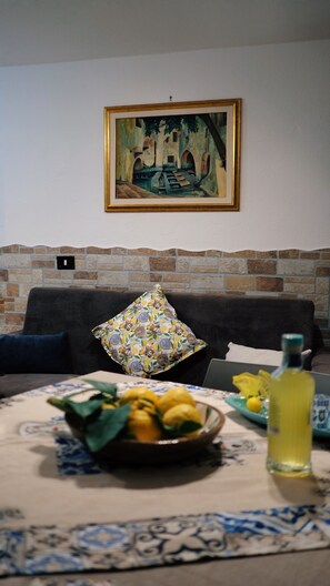 A living room with a sofa, a painting on the wall, a stone wall, a table with a bowl of lemons, and a bottle. - House of Gattopardo Cefalù (Cefalù)