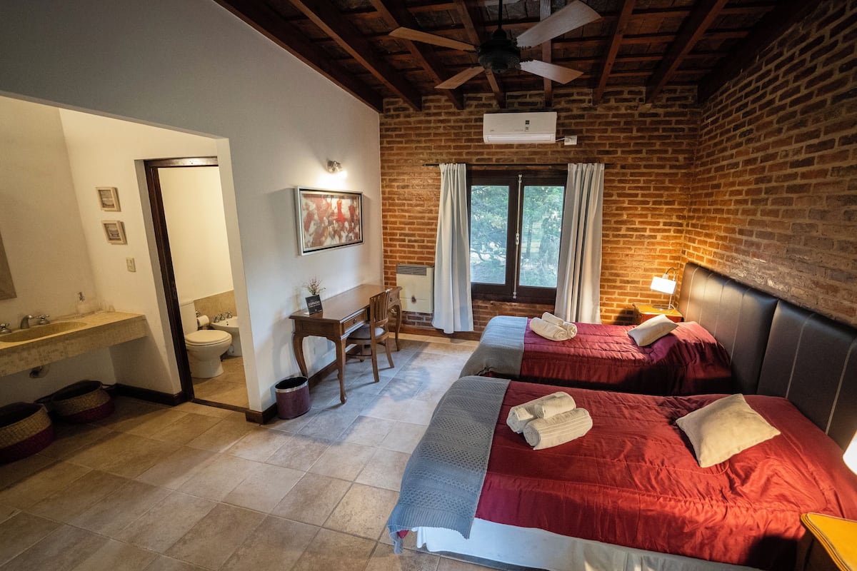 A hotel room with two beds, a bathroom, a desk, and a window with curtains.