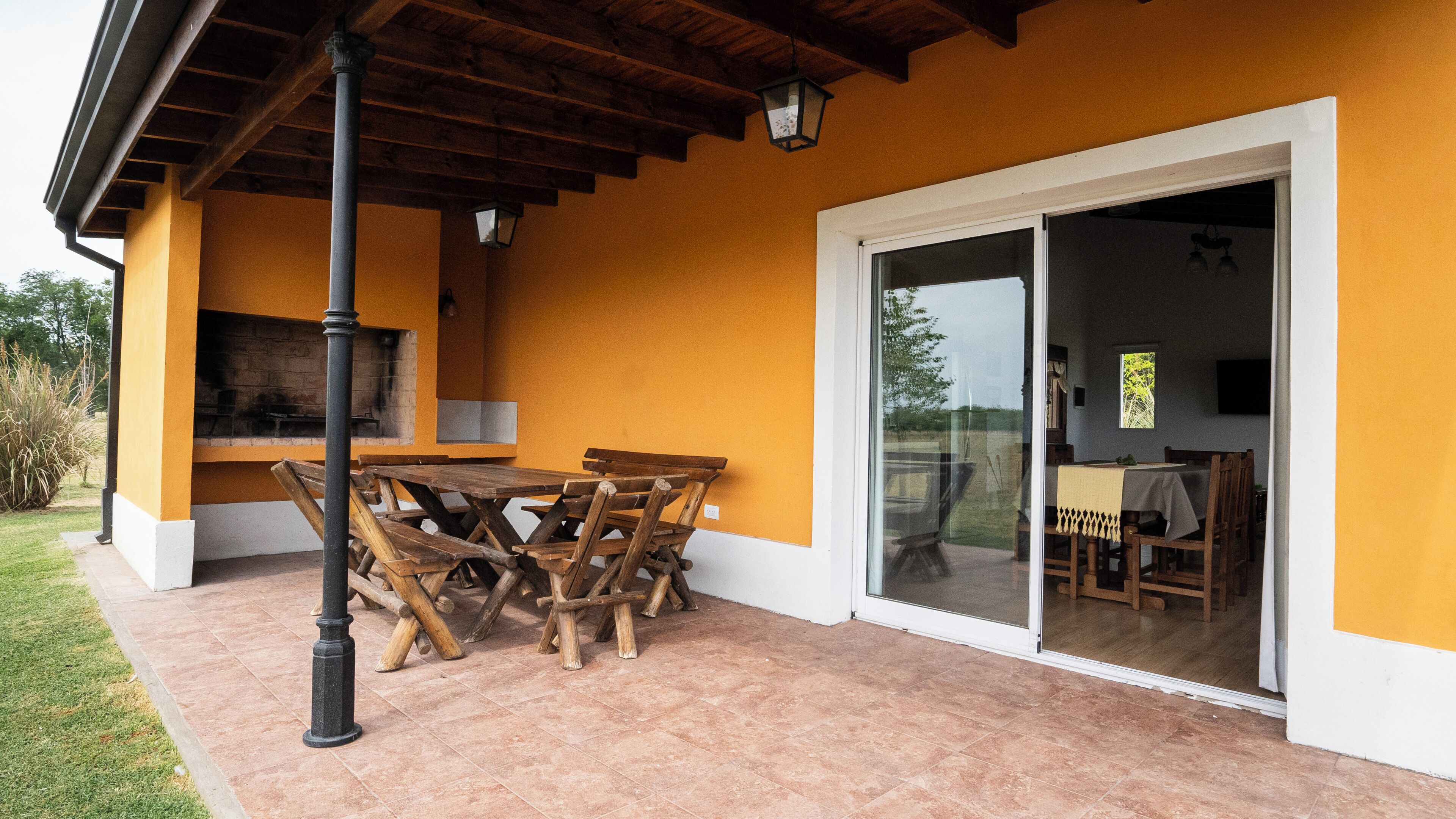 An outdoor patio with a wooden table and chairs, a grill, and a sliding glass door leading to an indoor dining area.