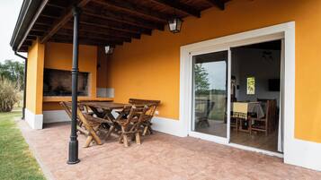 An outdoor patio with a wooden table and chairs, a grill, and a sliding glass door leading to an indoor dining area.