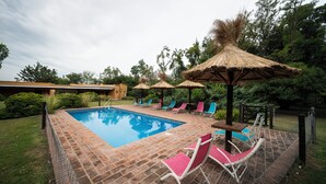 A swimming pool with lounge chairs and thatched umbrellas. - La Soleada Polo Ranch (Mercedes)