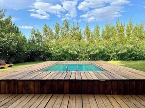 A rectangular swimming pool with a wooden deck surrounding it, set against a backdrop of dense green foliage and a clear blue sky. - LUX 7BA/5BA Oasis w/Heated Pool & Spa +huge garden (Las Vegas)