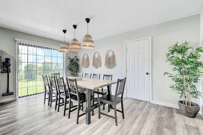 A dining area with a wooden table and chairs, pendant lights, a potted plant, and a view through a large window. - LUX 7BA/5BA Oasis w/Heated Pool & Spa +huge garden (Las Vegas)