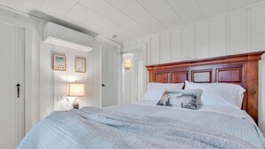 Ein Schlafzimmer mit einem großen Bett, weißen Wänden, einem Holzkopfende und einem Nachttisch mit Lampe.