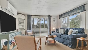Ein Wohnzimmer mit einer Couch, einem Fernseher, einem Sessel, einem Tisch und einem Schrank.