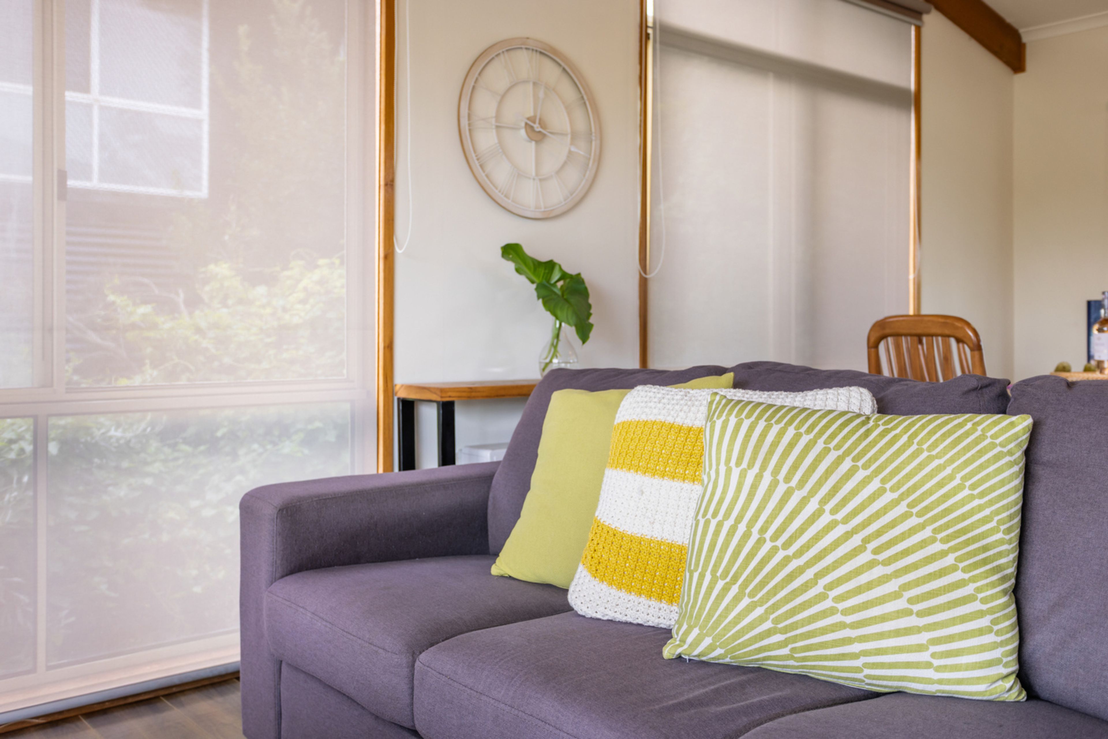 A living room with a sofa, a clock on the wall, and a plant.