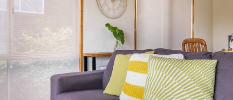 A living room with a sofa, a clock on the wall, and a plant.