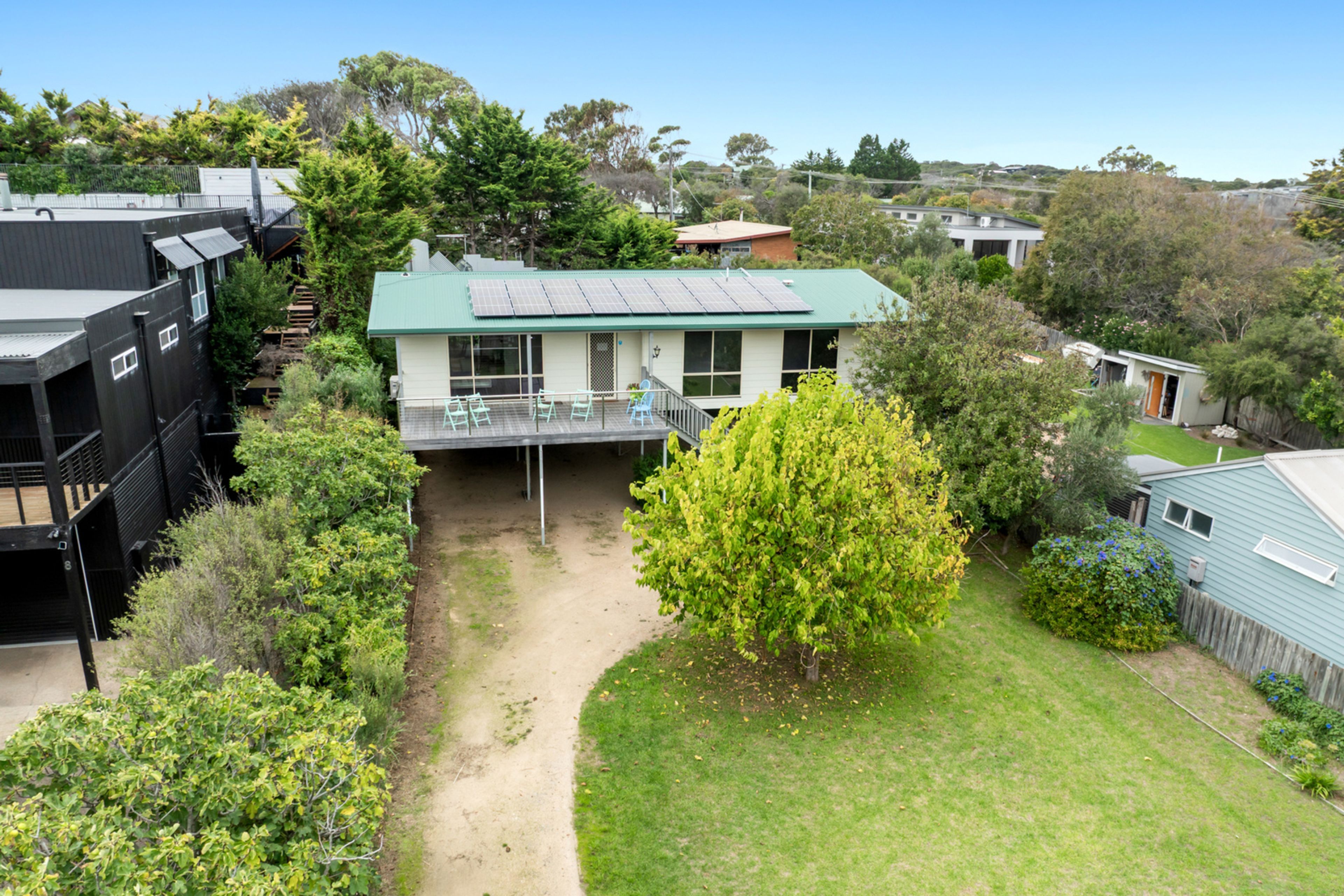 A residential property with a green-roofed house, a visible deck, and a surrounding garden.