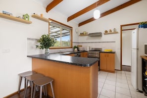 A kitchen with a central island, bar stools, a window, and a refrigerator. - Velora Rye Pet Friendly Home (Rye)