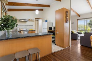 A modern kitchen with a central island, wooden beams, and a view to a living area with a sofa. - Velora Rye Pet Friendly Home (Rye)