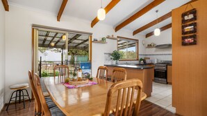 A dining area with a wooden table and chairs, a kitchen with a stove and oven, and a large window with a view of greenery. - Velora Rye Pet Friendly Home (Rye)