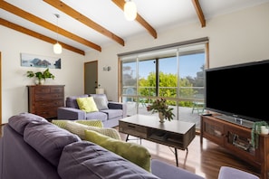 A modern living room with a large flat-screen TV, a sofa, a coffee table, and a wooden cabinet.