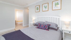 A bedroom with a bed, bedside tables, and framed botanical prints on the wall. - 204 Jefferson Ave (Cape Canaveral)