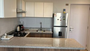 A modern kitchen with a granite countertop, stainless steel appliances, wooden cabinets, and two bar stools. - APARTMENT IN PIURA WITH PARK VIEW (Piura)