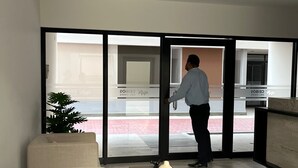 A modern living room with a sofa, a small table with a vase, and a person opening a glass door leading outside. - APARTMENT IN PIURA WITH PARK VIEW (Piura)