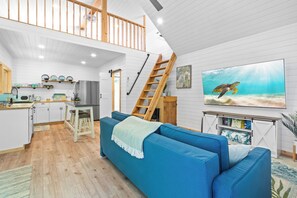 A modern interior with a loft bedroom, a kitchen, and a living area featuring a large TV. - The Palm (Palm Bay)
