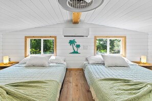 Une chambre avec deux lits, un ventilateur de plafond, un appareil de climatisation et des fenêtres donnant sur un paysage verdoyant.