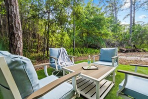 Un espace extérieur aménagé avec deux chaises et une table, entouré d’arbres et de verdure.