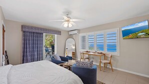Ein Schlafzimmer mit Bett, Deckenventilator, Fenster mit Rollläden, Esstisch mit Stühlen und Meerblick.