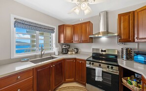 A kitchen with wooden cabinets, a stainless steel range, a built-in oven, a coffee maker, and a window with a view. - Affordable-Cozy-Views | 5 mins to Magens Bay (St Thomas)
