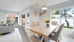 A modern dining area with a wooden table and grey upholstered chairs, a pendant light, and a vase of flowers. - Remuera 3BR Elegance Home with Outdoor Living (Auckland Central Suburbs)
