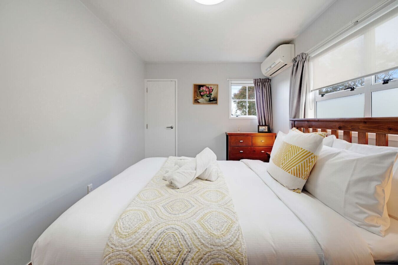 A bedroom with a bed, a wooden nightstand, a window with curtains, and a door.