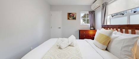 A bedroom with a bed, a wooden nightstand, a window with curtains, and a door.
