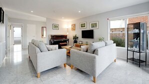 A modern living room with a piano, sofas, a TV, and a glass display unit. - Remuera 3BR Elegance Home with Outdoor Living (Auckland Central Suburbs)