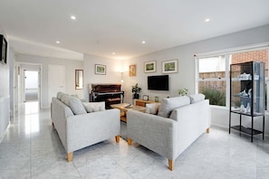 A modern living room with a piano, sofas, a TV, and a glass display unit. - Remuera 3BR Elegance Home with Outdoor Living (Auckland Central Suburbs)
