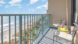 Un balcón con vista a la playa, una silla, una mesa y una botella de vino.