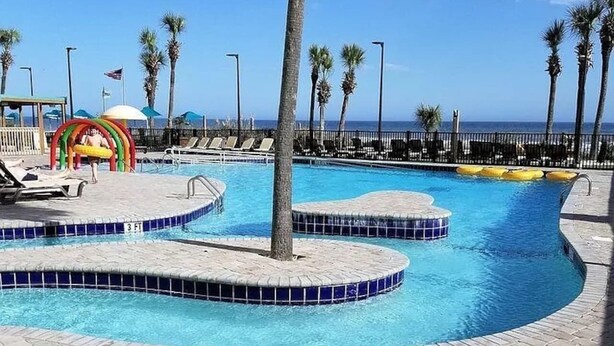 Una piscina con borde curvo, palmeras y vista al océano.