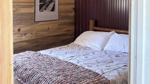 Une chambre avec un mur en bois, un tableau encadré, un lit avec une literie blanche et une couverture tricotée.