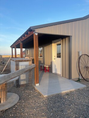 A building with a covered porch, a door, and a large wheel.