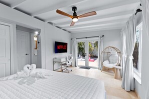 A bedroom with a bed, a desk, a chair, a ceiling fan, a TV, and a view of the outside. - Mid-Century Pool Oasis | Hot Tub | Near Beach (Wilton Manors)
