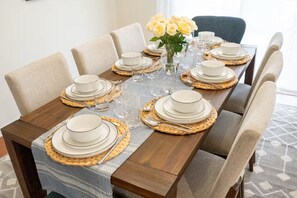 A dining table set with white plates, bowls, and glasses, surrounded by chairs. - 3BR Beach House for 8 Game Room & Fire Pit (Rehoboth Beach)