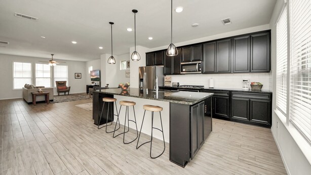 Una cocina moderna con armarios oscuros, una isla central con taburetes, un microondas y un refrigerador.