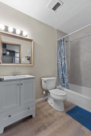 Ein Badezimmer mit Waschtisch, Toilette, Dusche und einem beleuchteten Spiegel.