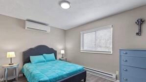 A bedroom with a bed, bedside tables, a dresser, a window with blinds, an air conditioning unit, and a decorative key on the wall. - Quiet 1BR for Two · Tower Grove · Pet-Friendly · Free Parking + Laundry (St. Louis)