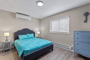 Ein Schlafzimmer mit Bett, Nachttischen, Kommode, Fenster mit Jalousien, Klimaanlage und einem dekorativen Schlüssel an der Wand.