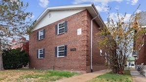 A two-story brick building with a flat roof, a small front yard, and a tree with autumn leaves. - Quiet 1BR for Two · Tower Grove · Pet-Friendly · Free Parking + Laundry (St. Louis)