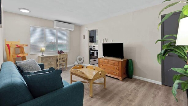 A living room with a sofa, a wooden coffee table, a TV, a dining area with a table and chairs, and a kitchen area with a microwave and oven. - Quiet 1BR for Two · Tower Grove · Pet-Friendly · Free Parking + Laundry (St. Louis)