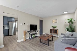 Una sala de estar moderna con un sofá gris, una mesa de centro, un televisor y una cocina al fondo.